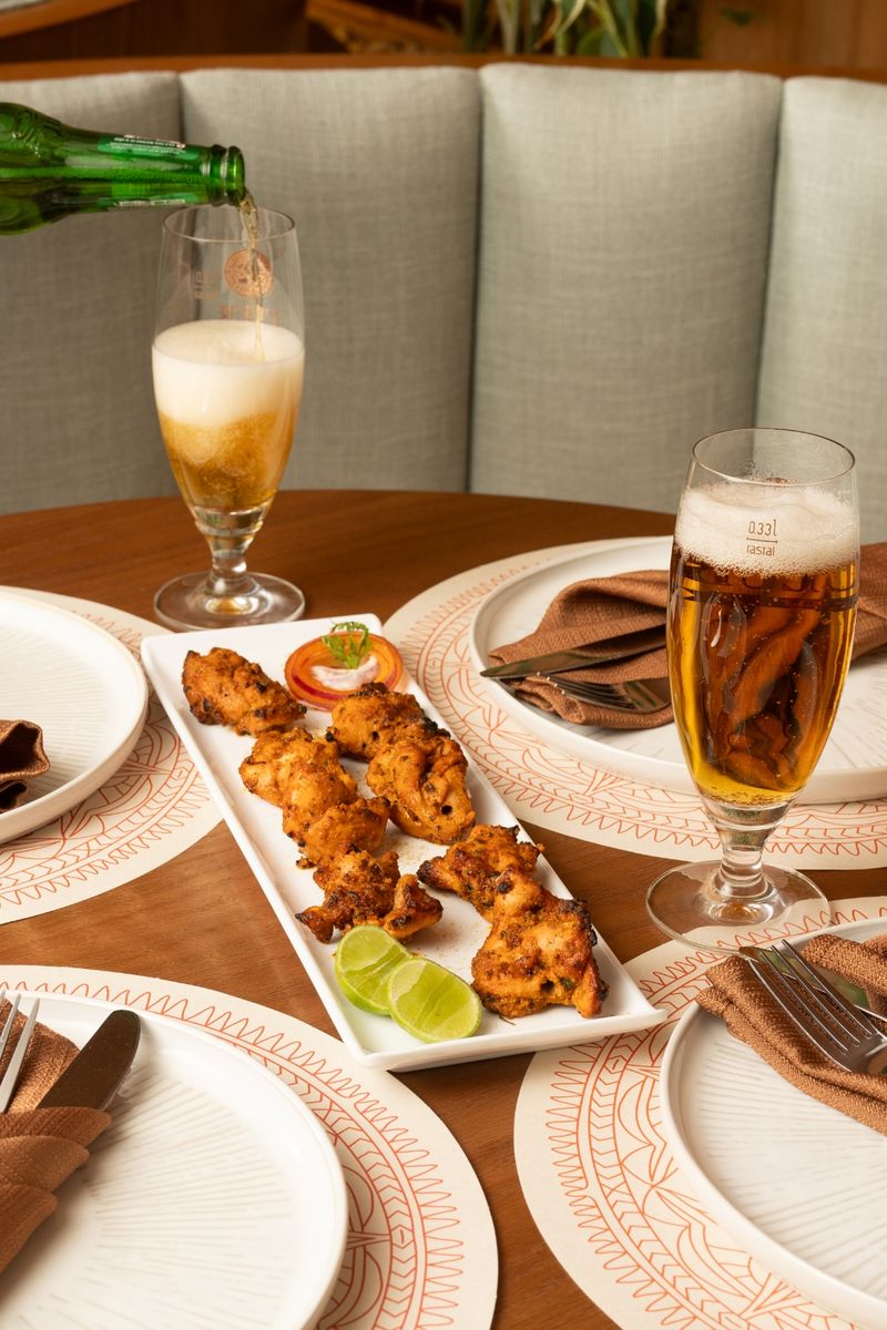 Chicken tikka skewers with lime, and a cold beer being poured tableside