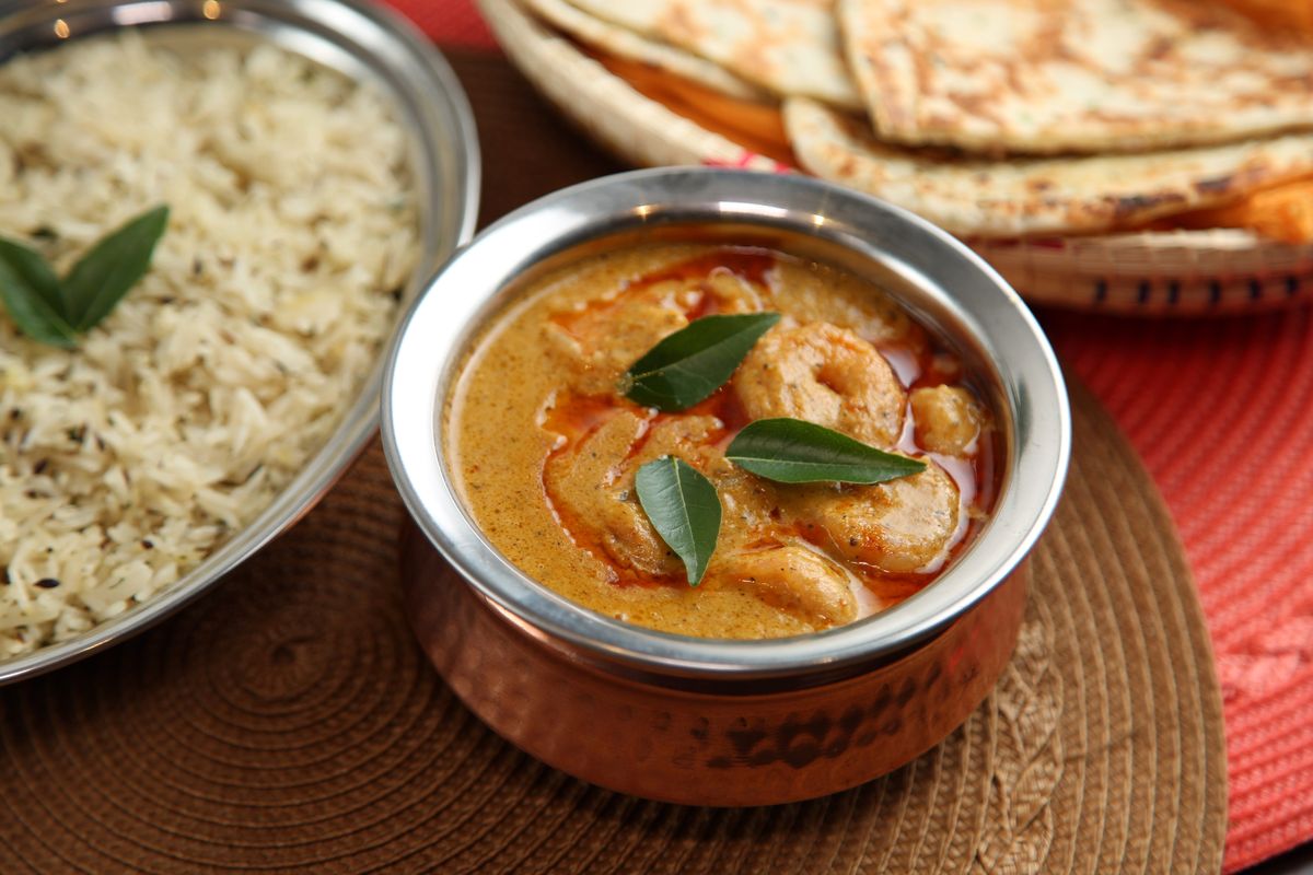 Goan-style prawn curry garnished with curry leaves, served with naan and rice